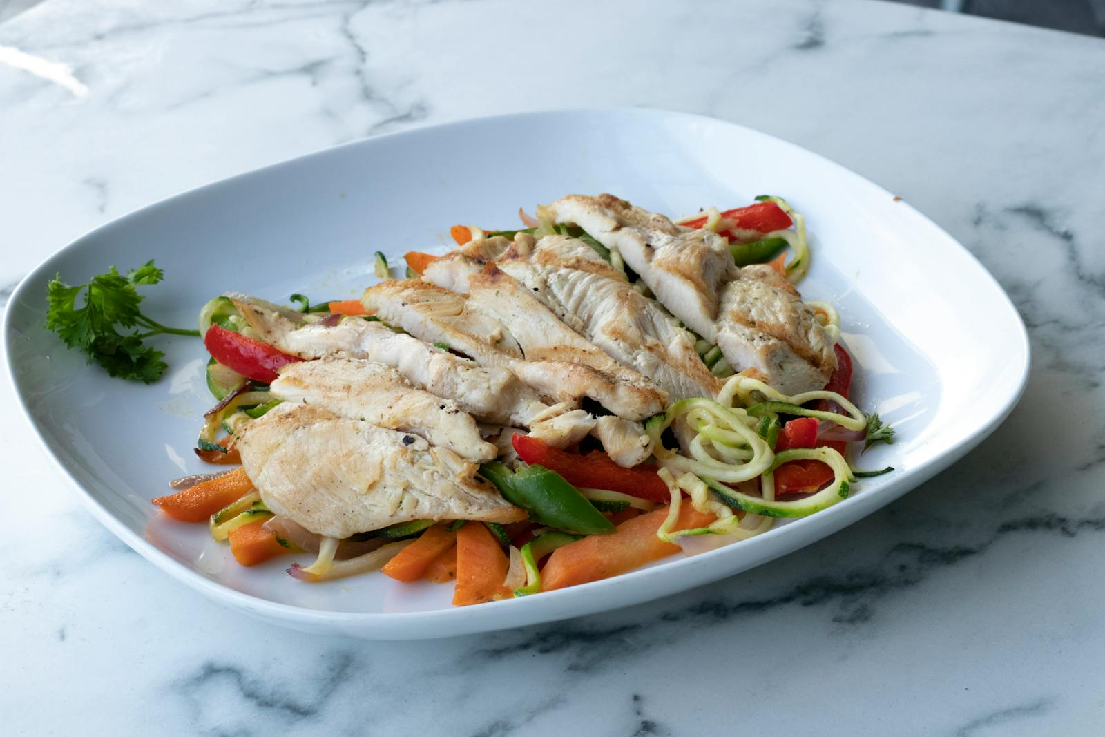 Healthy grilled chicken breast served on zucchini noodles and fresh vegetables.