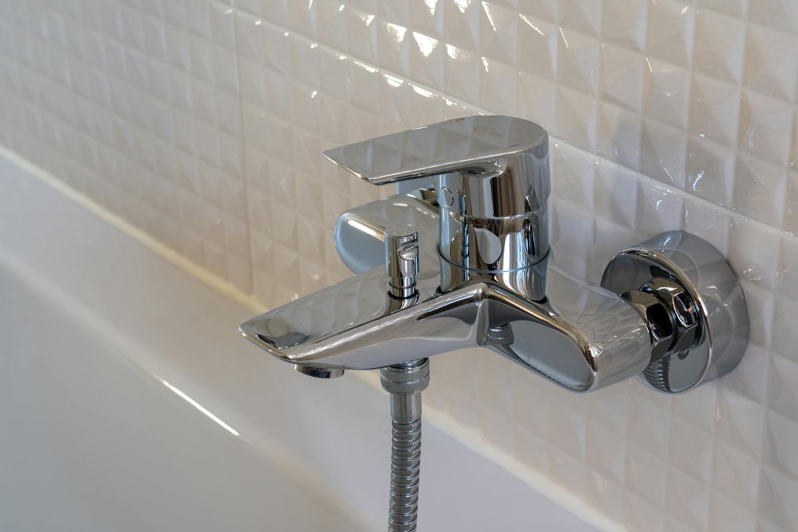 Close-up of a contemporary chrome faucet in a modern bathroom with white geometric tiles.
