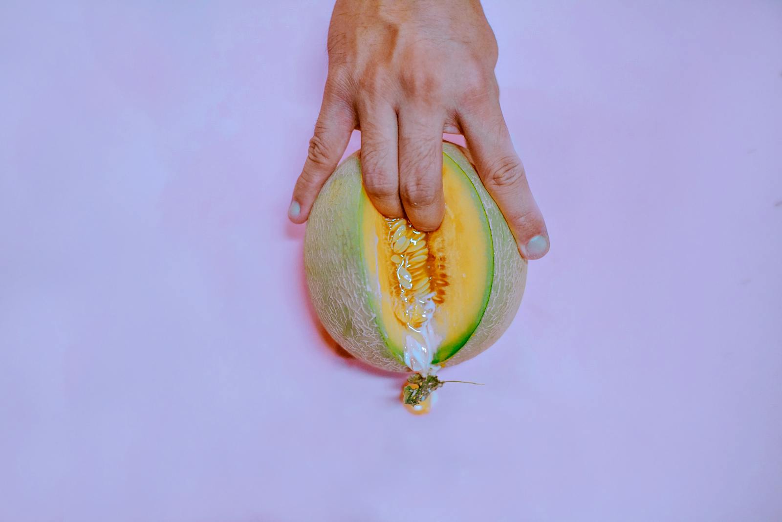 How to Increase Your Sex Drive Naturally 1 A hand gently touches a ripe melon on a pastel pink backdrop, creating a vivid and conceptual image.