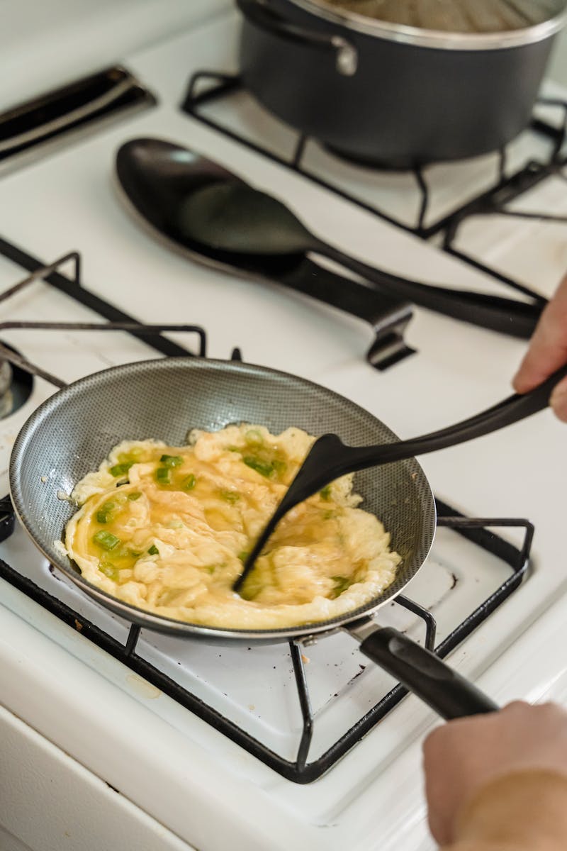 Person cooking scrambled eggs in a pan on a stove. Home kitchen setting.
