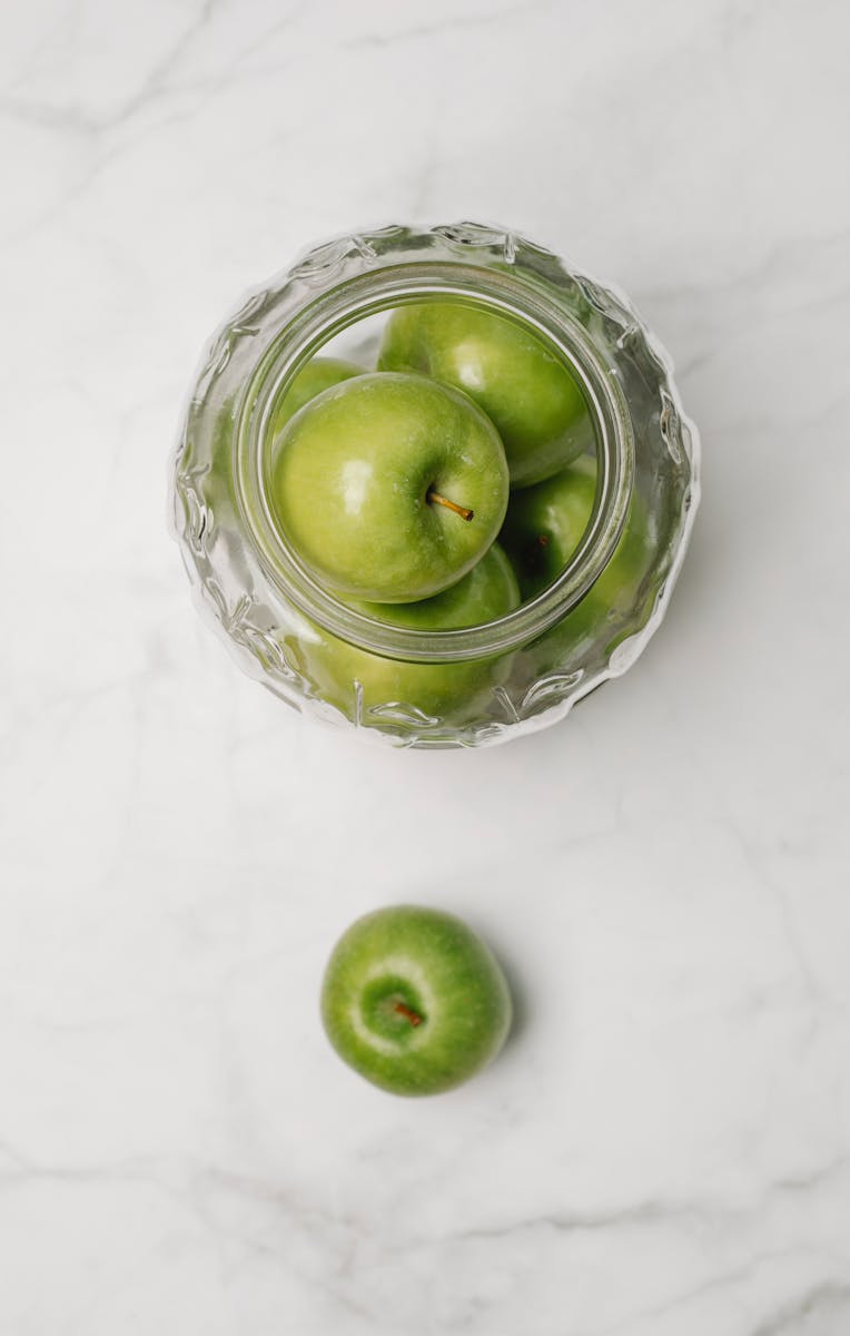 Top view of fresh green apples in a crystal bowl on a marble background, perfect for healthy eating concepts.