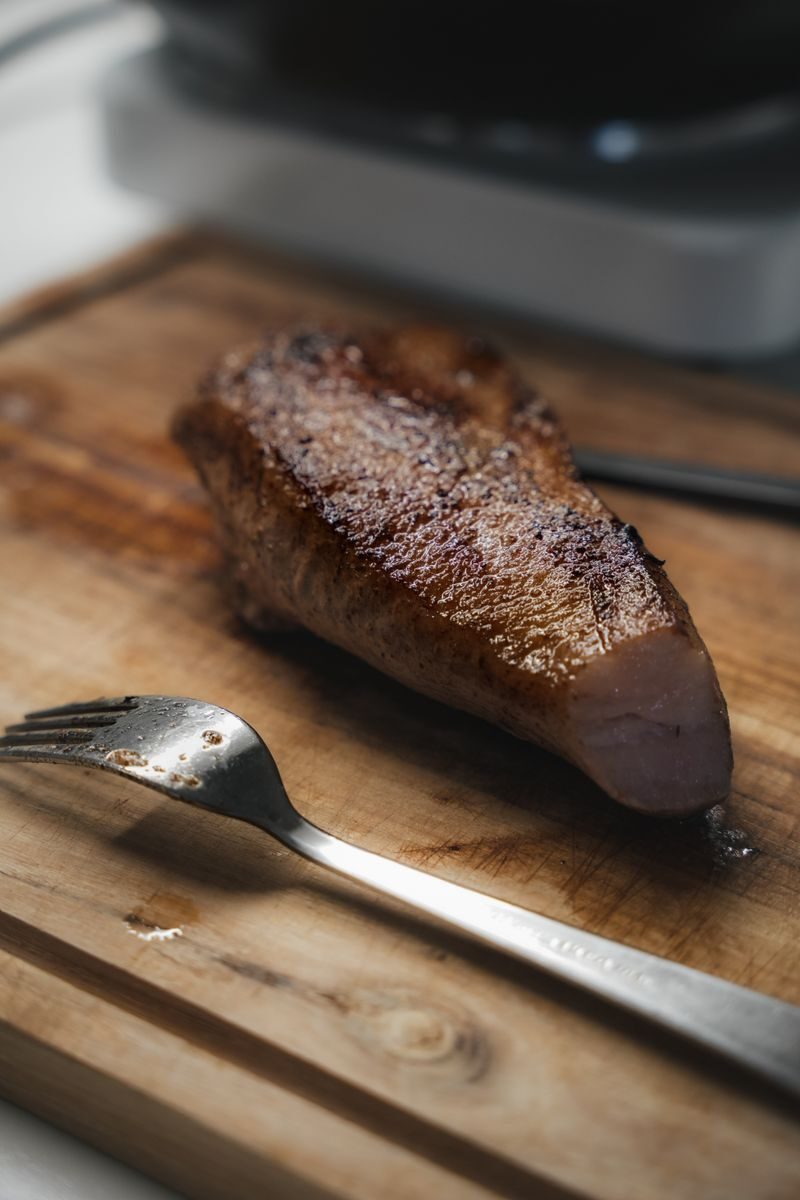 Deliciously seared pork piece resting on a wooden board in natural light.